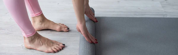 Partial view of barefoot woman unrolling yoga mat on floor at home, banner — Stock Photo