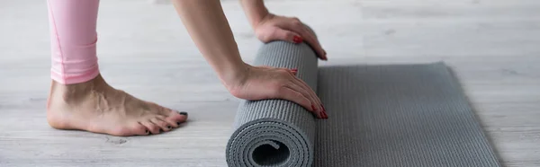 Cropped view of barefoot woman unrolling yoga mat on floor, banner — Stock Photo