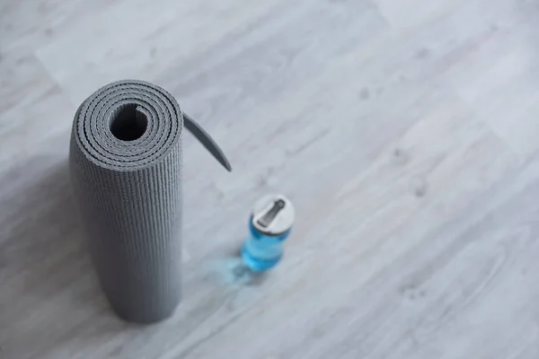 Sélectif de tapis de fitness roulé près de la bouteille de sport avec de l'eau — Photo de stock