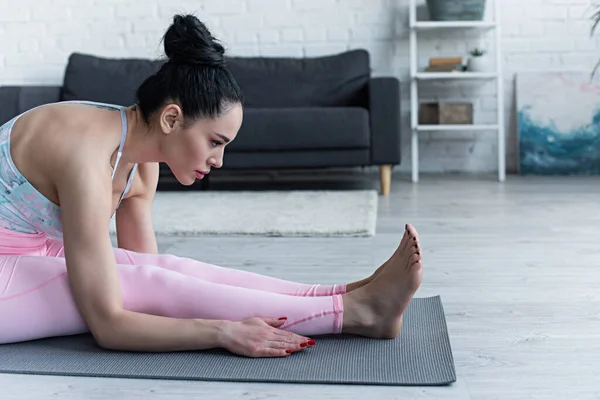 Barefoot woman practicing seated forward bend pose at home — Stock Photo