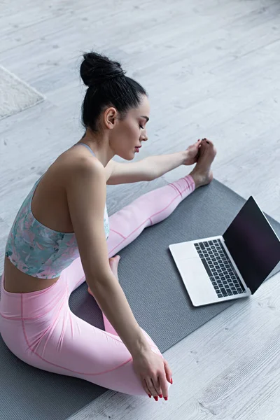 Mulher esportiva alongamento em ioga pose perto de laptop com tela em branco — Fotografia de Stock