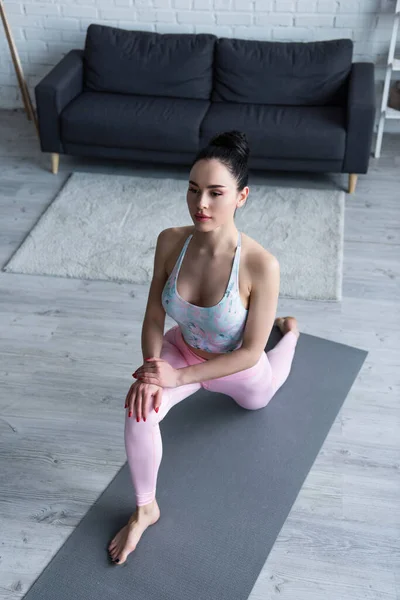 Vista de ángulo alto de la mujer descalza que practica la embestida en la postura de la rodilla en la esterilla de yoga - foto de stock