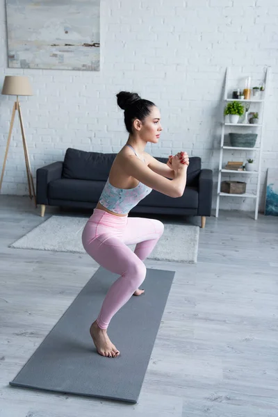 Bonita mujer de pie en silla posan con las manos apretadas mientras practica yoga en casa - foto de stock