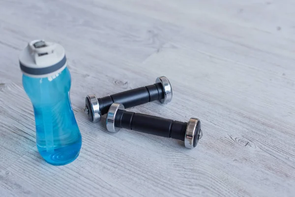 Sports bottle with water near dumbbells on floor — Stock Photo