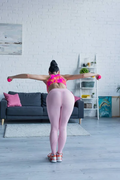 Vista posteriore di giovane donna in leggings formazione con manubri a casa — Foto stock