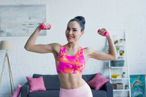 Mujer deportiva sonriendo a la cámara mientras hace ejercicio con pesas en casa - foto de stock