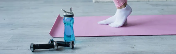 Vista recortada de la mujer en calcetines en la estera de fitness cerca de pesas y botellas deportivas, pancarta - foto de stock