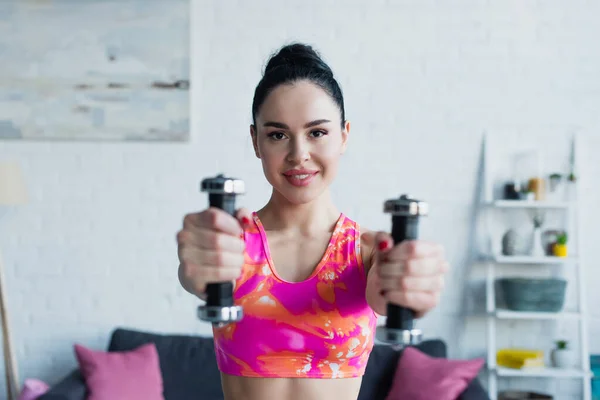 Mujer alegre sonriendo a la cámara mientras hace ejercicio con pesas - foto de stock