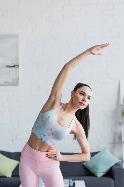 Jolie femme en soutien-gorge de sport faire un exercice de flexion latérale avec la main levée — Photo de stock