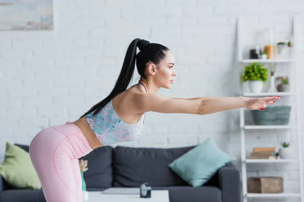 Side view of brunette woman in sportswear doing forward bend exercise with outstretched hands — Stock Photo