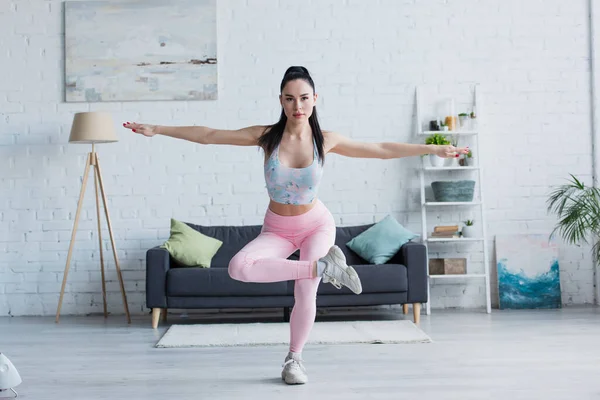 Young sportswoman looking at camera while standing in tree pose at home — Stock Photo