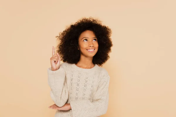 Afroamericana preadolescente chica apuntando hacia arriba con el dedo aislado en beige - foto de stock