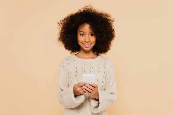 Sorridente africana americana preteen menina com segurando smartphone em mãos isoladas no bege — Fotografia de Stock
