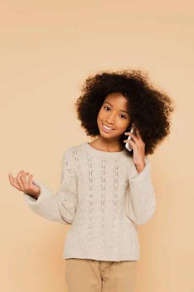 Africano americano preteen ragazza parlando su cellulare e gesticolando con mano isolato su beige — Foto stock