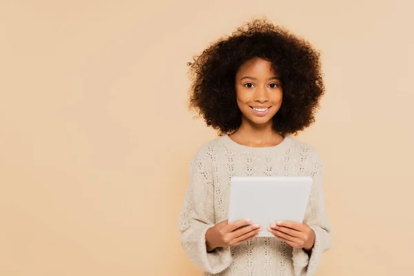 Africana americana preteen menina olhando para a câmera com tablet em mãos isoladas no bege — Fotografia de Stock