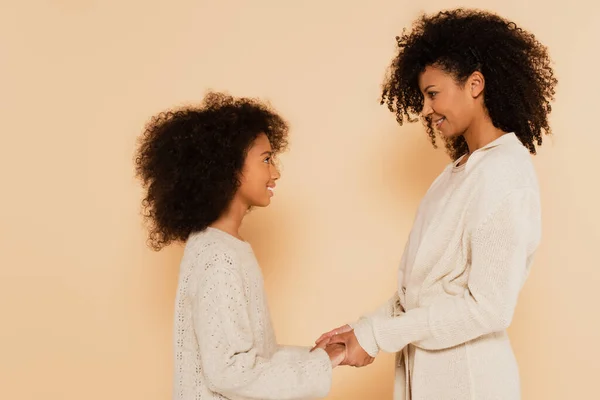 Afro-americano preteen filha ternamente de mãos dadas com a mãe no fundo bege — Fotografia de Stock