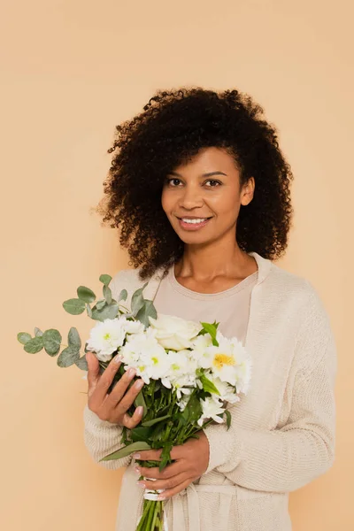 African american woman holding bouquet of daisies and looking at camera isolated on beige — Stock Photo