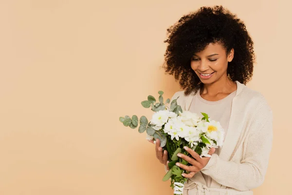 African american woman holding bouquet of daisies and smiling on beige background — Stock Photo