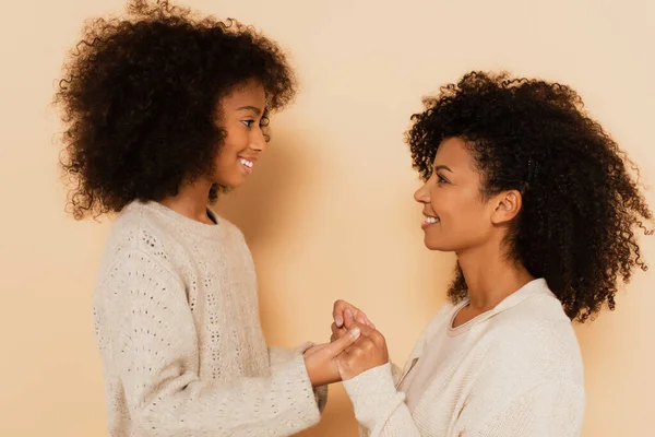 Seitenansicht der afrikanisch-amerikanischen Preteen-Tochter und erwachsenen Mutter Händchen haltend auf beigem Hintergrund — Stockfoto