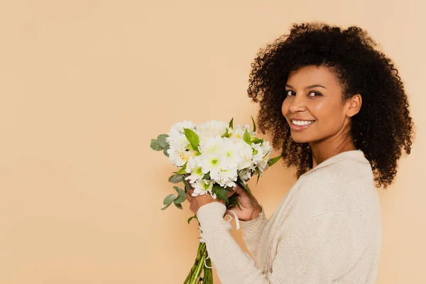 African american woman holding bouquet of daisies and smiling isolated on beige — Stock Photo