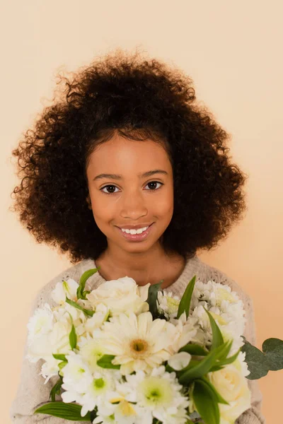 Portrait of smiling african american preteen girl with bouquet of flowers in hands isolated on beige — Stock Photo