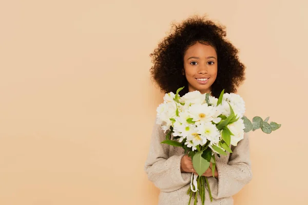 Smiling african american preteen girl with bouquet of flowers in hands isolated on beige — Stock Photo