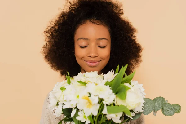 Happy preteen african american girl smelling bouquet of daisies with closed eyes isolated on beige — Stock Photo