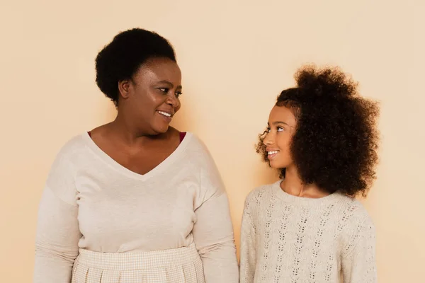 African american grandmother and granddaughter looking at each other on beige background — Stock Photo