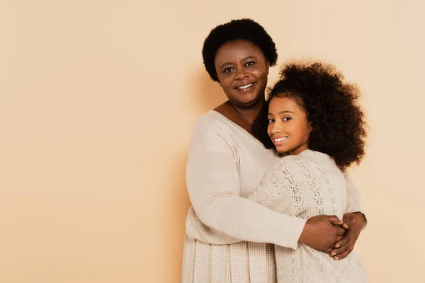 Smiling african american grandmother hugging granddaughter on beige background — Stock Photo