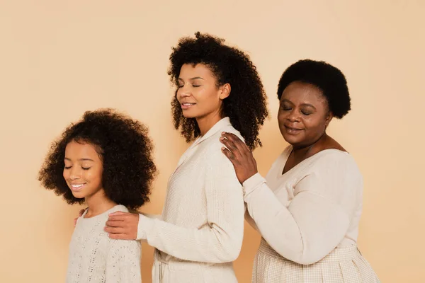 African american daughter, mother and grandmother holding hands on shoulders of each other isolated on beige — Stock Photo