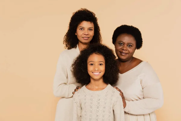 Familia sonriente de madre afroamericana, abuela y nieta aisladas en beige - foto de stock