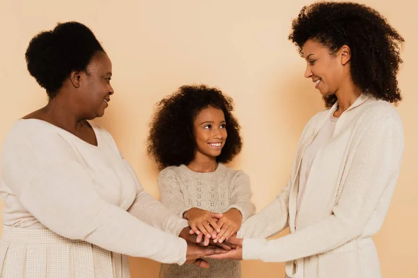African american grandmother, mother, daughter holding hands together on beige background — Stock Photo