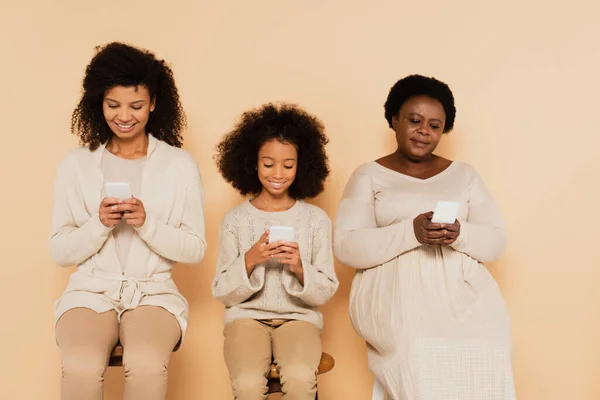 Afro-americana filha, neta e avó sentado e olhando para celulares em fundo bege — Fotografia de Stock