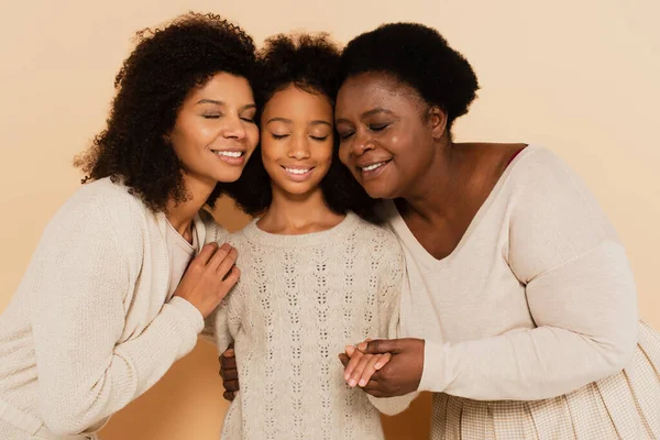 Afrikanisch-amerikanische Tochter, Enkelin und Großmutter umarmen Wangen an Wangen und halten Hände auf beigem Hintergrund — Stockfoto