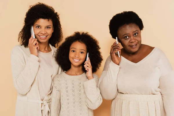 Афроамериканська дочка, онука і бабуся розмовляють на мобільних телефонах на бежевому фоні — стокове фото