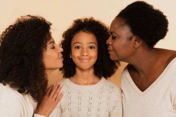 African american daughter and grandmother kissing granddaughter granddaughter with closed eyes on beige background — Stock Photo