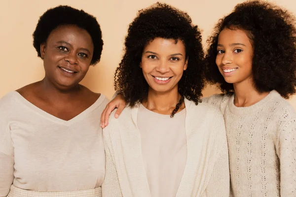 Sonriente afroamericana abuela, hija, nieta mirando a la cámara sobre fondo beige - foto de stock