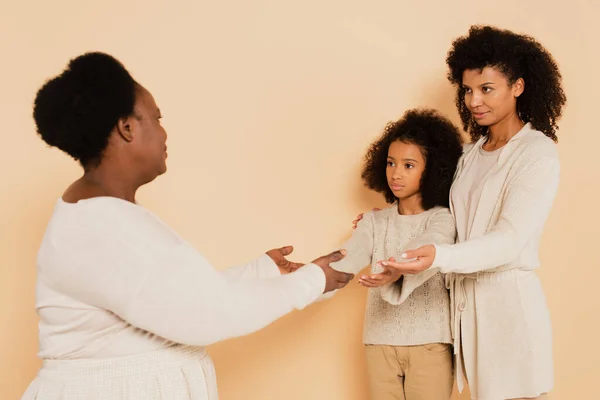 Afro-americana mãe com filha colocando as mãos estendidas para avó no fundo bege — Fotografia de Stock