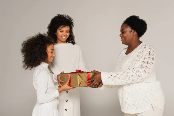Веселая африканская бабушка-американка подарила подарочную коробку дочери и внучке на сером фоне — стоковое фото