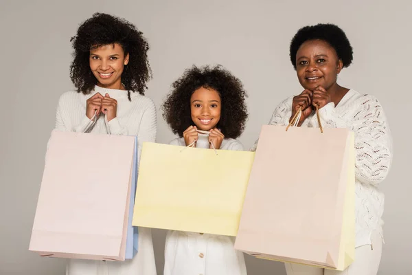 Возбужденная африканская американская мать, дочь и бабушка держат сумки с покупками на сером фоне — стоковое фото