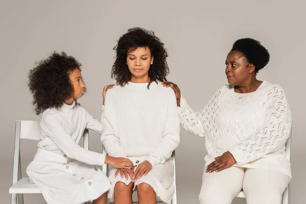 Розчарована афроамериканська доросла жінка, що сидить між дев'ятнадцятьма дочками та матір'ю середнього віку ізольована на сірому — стокове фото