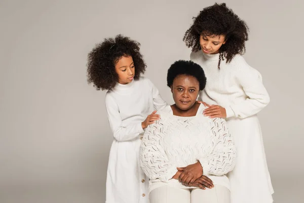 Afrikanisch-amerikanische Tochter und Mutter umarmen Großmutter vorsichtig und betrachten sie isoliert auf grau — Stockfoto