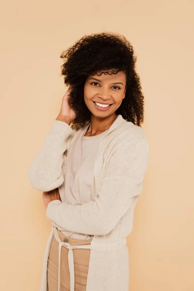 Atractiva mujer afroamericana ajustando el cabello aislado en beige - foto de stock