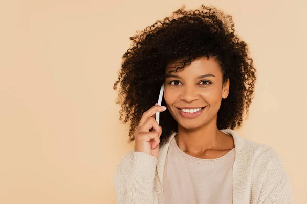 Glückliche afrikanisch-amerikanische Frau telefoniert und schaut vereinzelt in die Kamera auf beige — Stockfoto