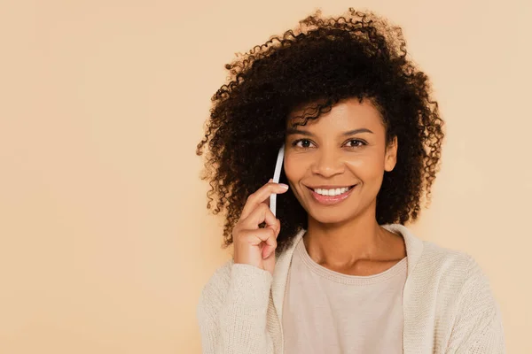 Feliz mulher afro-americana falando no celular e olhando para a câmera isolada no bege — Fotografia de Stock