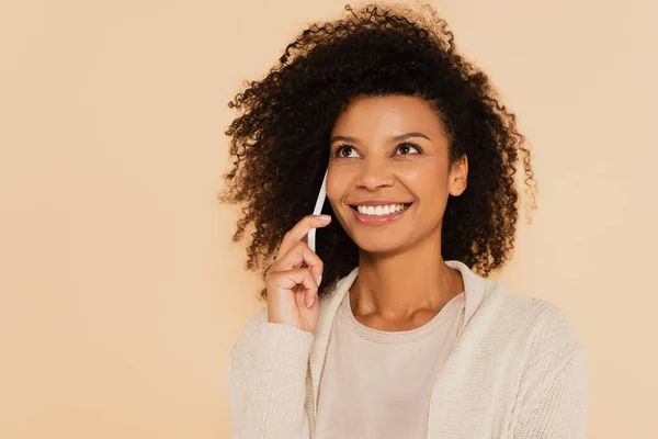 Happy african american woman speaking on cellphone and looking up isolated on beige — Stock Photo