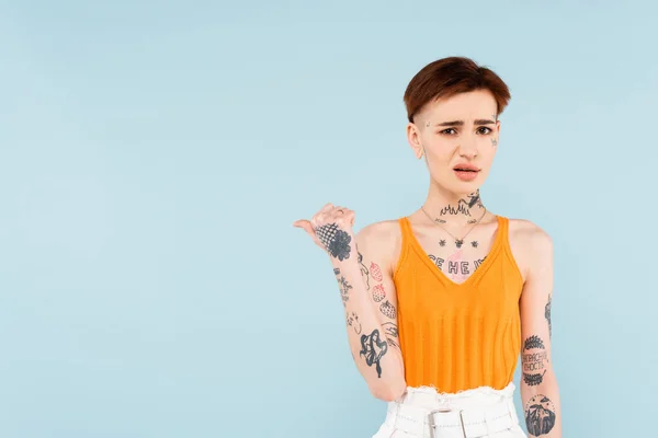 Descontente e tatuado mulher apontando com o polegar de distância isolado no azul — Fotografia de Stock
