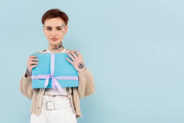 Junge tätowierte Frau hält umwickeltes Geschenk isoliert auf blauem Grund — Stockfoto