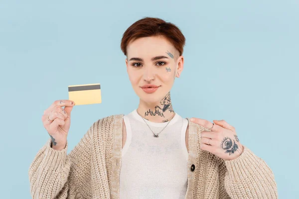 Donna allegra e tatuata che punta il dito sulla carta di credito isolata sul blu — Foto stock