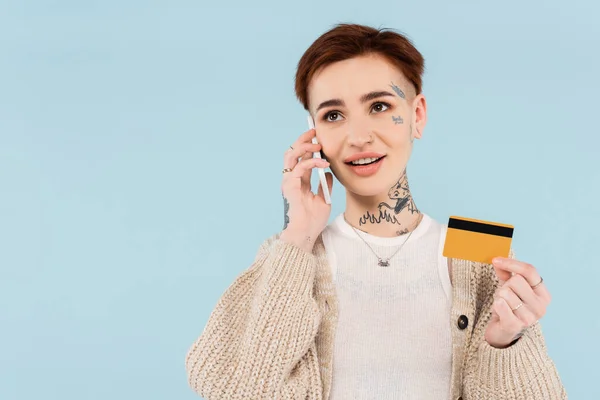 Mulher alegre e tatuado segurando cartão de crédito ao fazer a ordem no smartphone isolado no azul — Fotografia de Stock